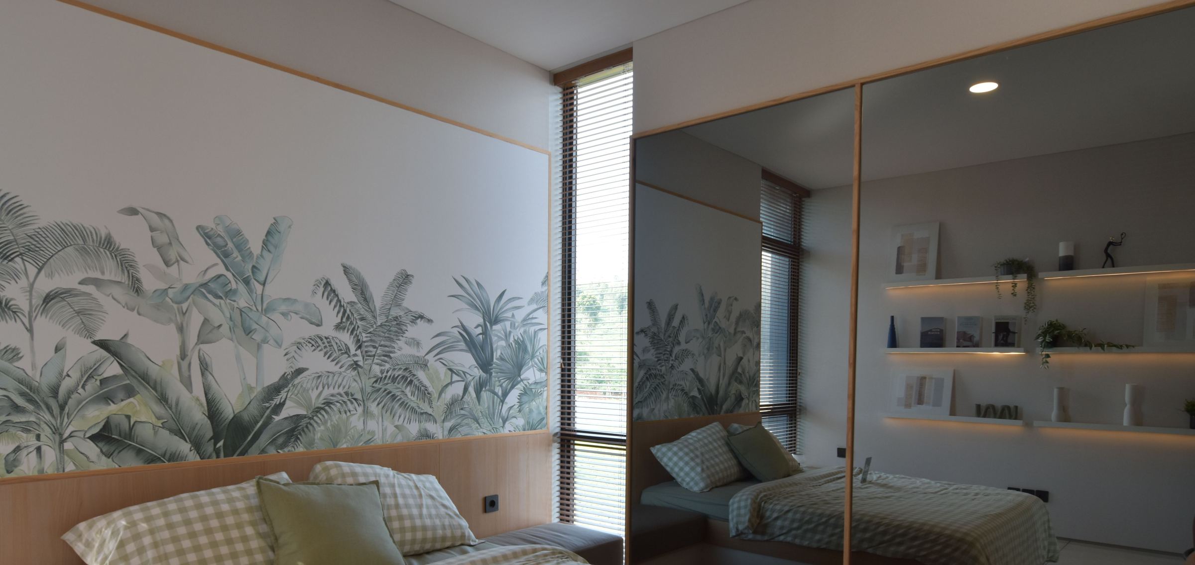 Bright bedroom with a sage-green botanical wallpaper mural above a light oak headboard, beside a tall window and mirrored wardrobe