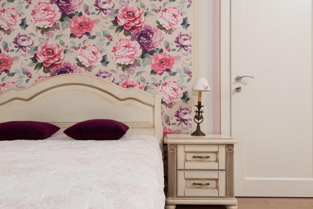 Bedroom with large pink and purple peony wallpaper behind a cream headboard and nightstand