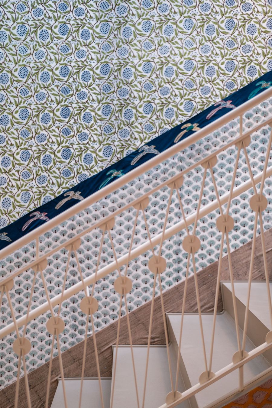 Stairway wall covered in a blue and green floral print wallpaper, seen at a diagonal along a cream railing