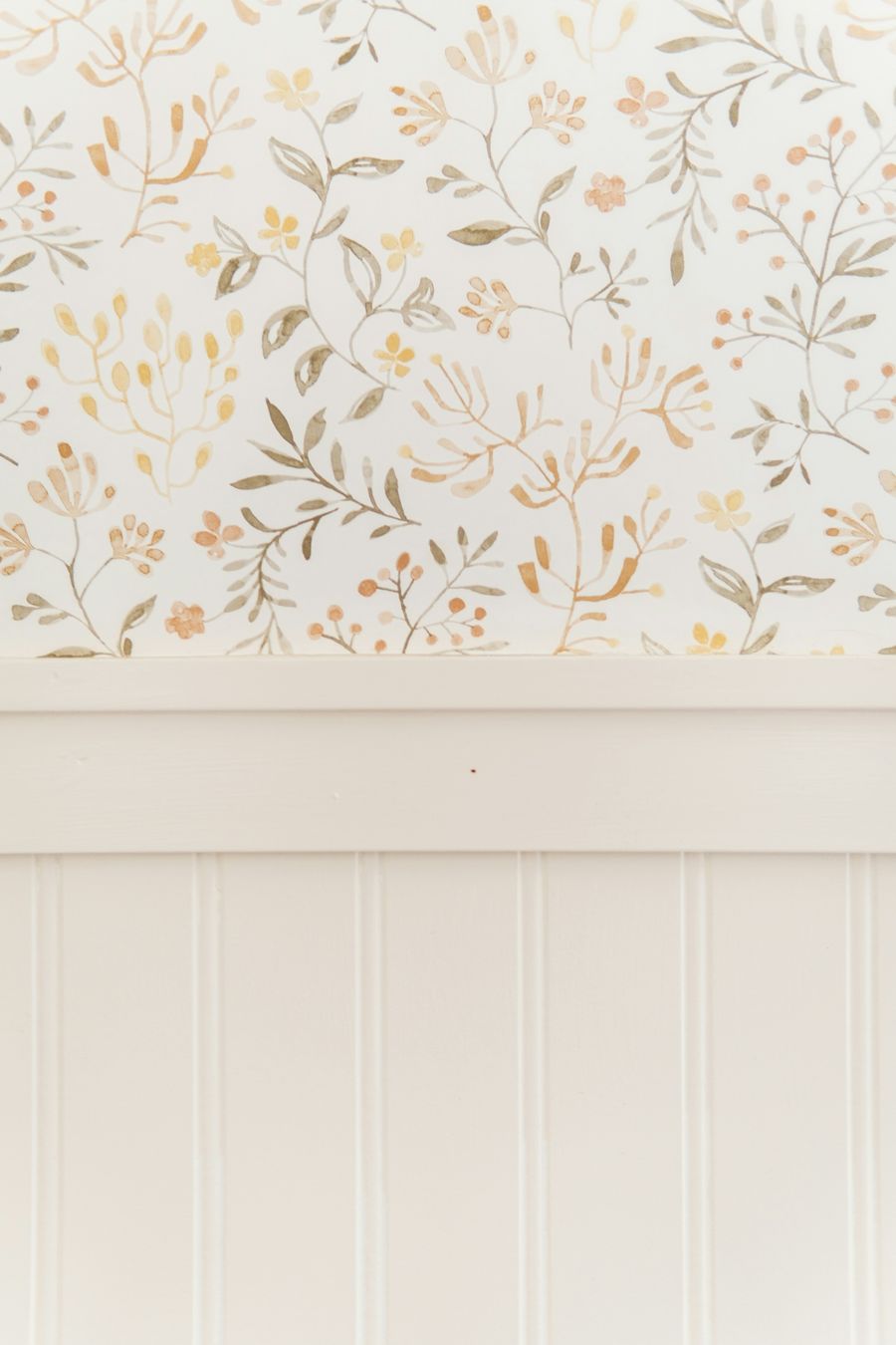 Soft floral wallpaper in muted gold and sage above white beadboard wainscoting